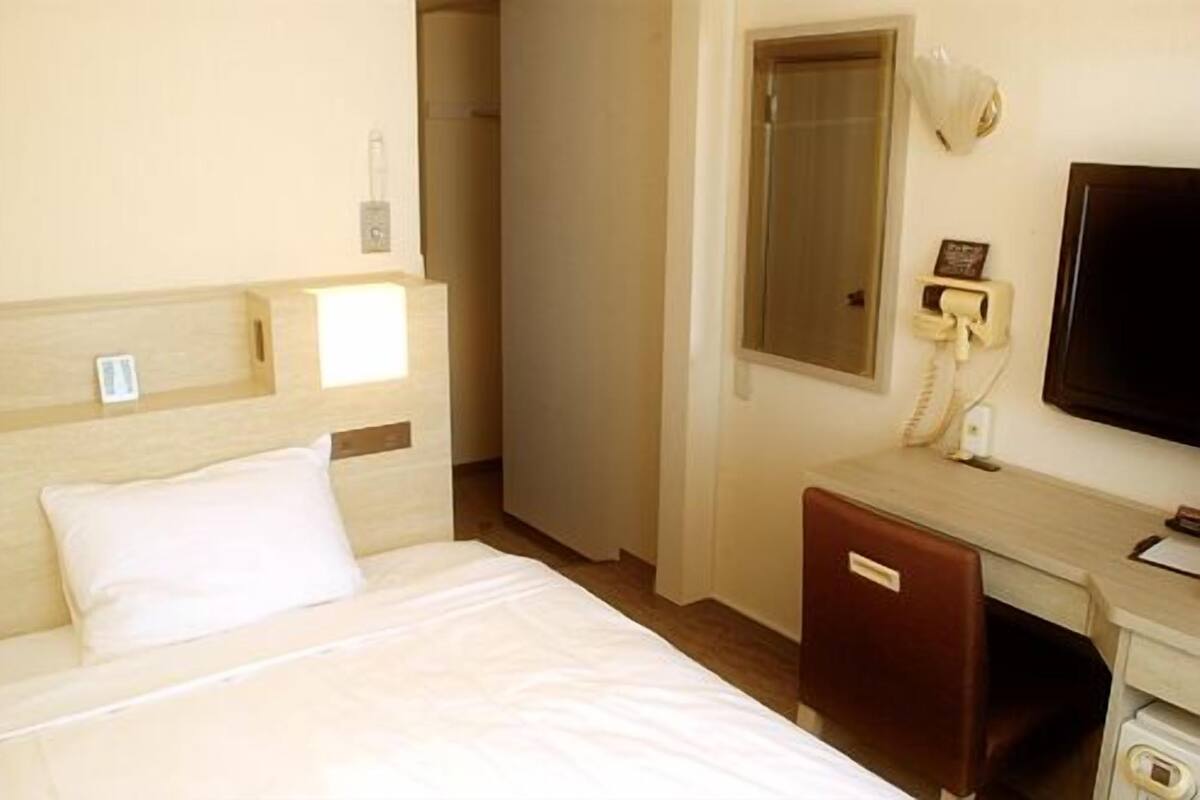 Una habitación de hotel con cama, escritorio, silla, teléfono y televisión.