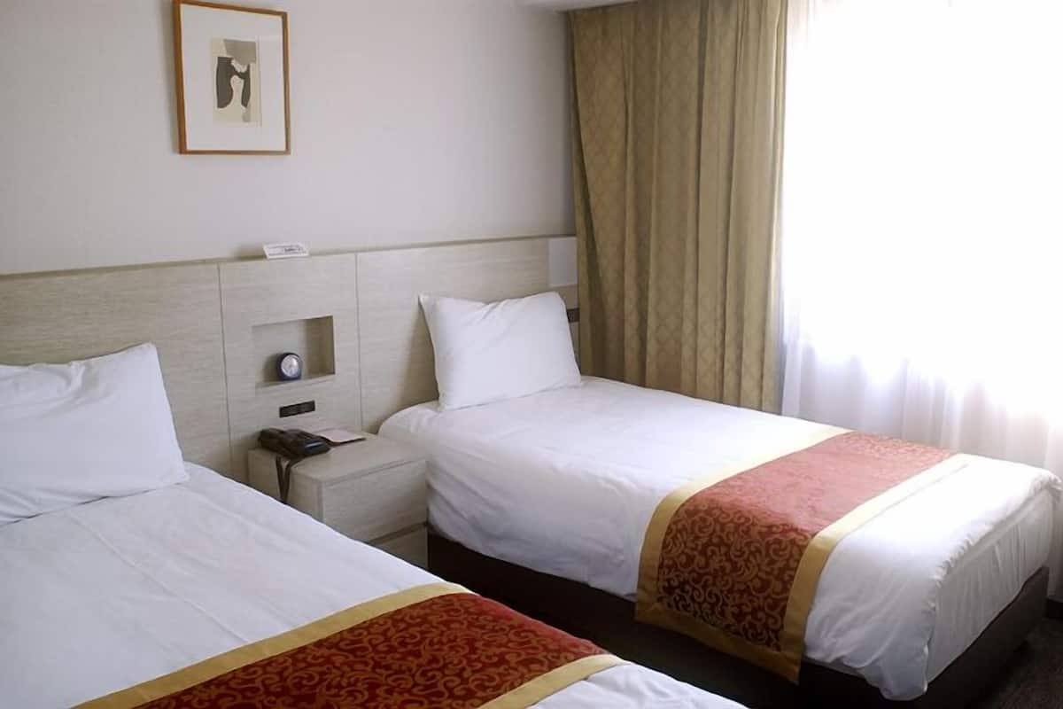 Habitación de hotel con dos camas, una mesita de noche con un teléfono, un estante pequeño y una ventana con cortinas.