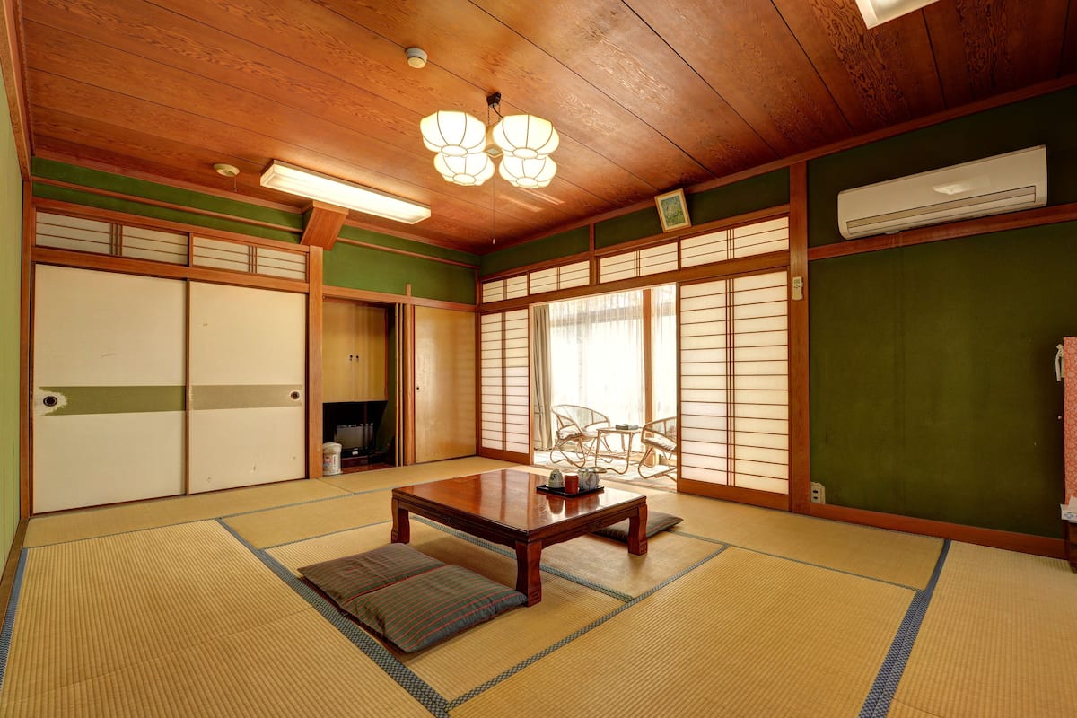 A traditional Japanese room with tatami flooring, a low wooden table, sliding doors, and a view through shoji screens.