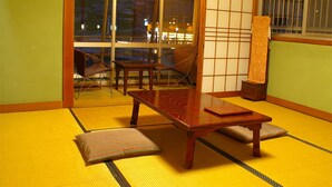 Une pièce avec un sol recouvert de tatamis, une petite table en bois, deux chaises, une porte coulissante et un paravent japonais traditionnel.