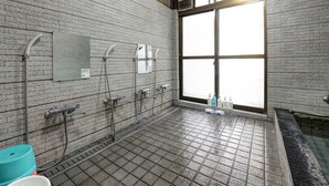 Des toilettes publiques avec un sol carrelé, une grande fenêtre et un espace douche.