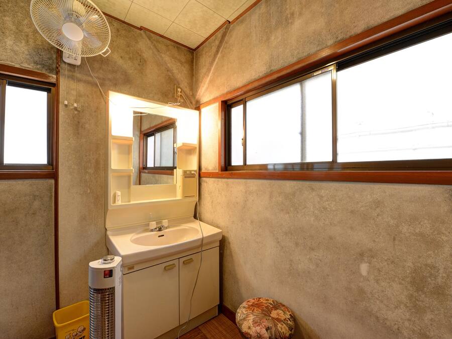 A bathroom with a large mirror, a sink, a toilet, a fan, and a window.