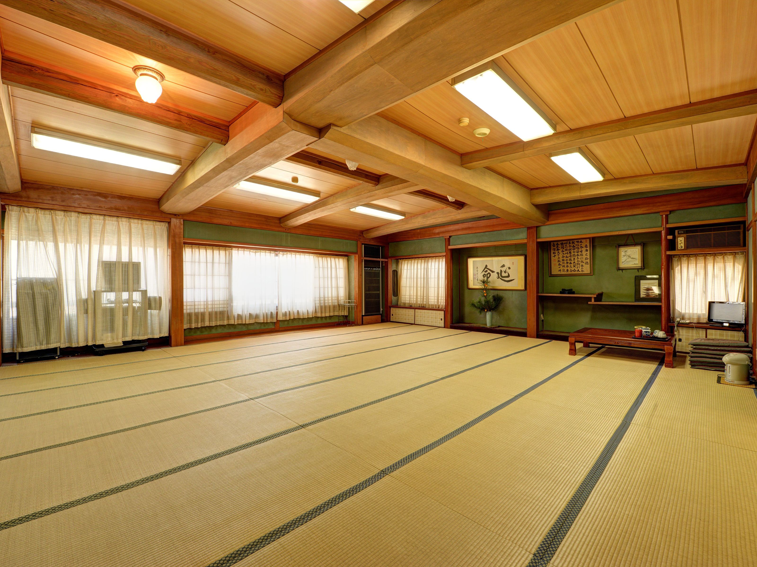 A traditional Japanese room with tatami flooring, wooden beams, sliding doors, and a television.