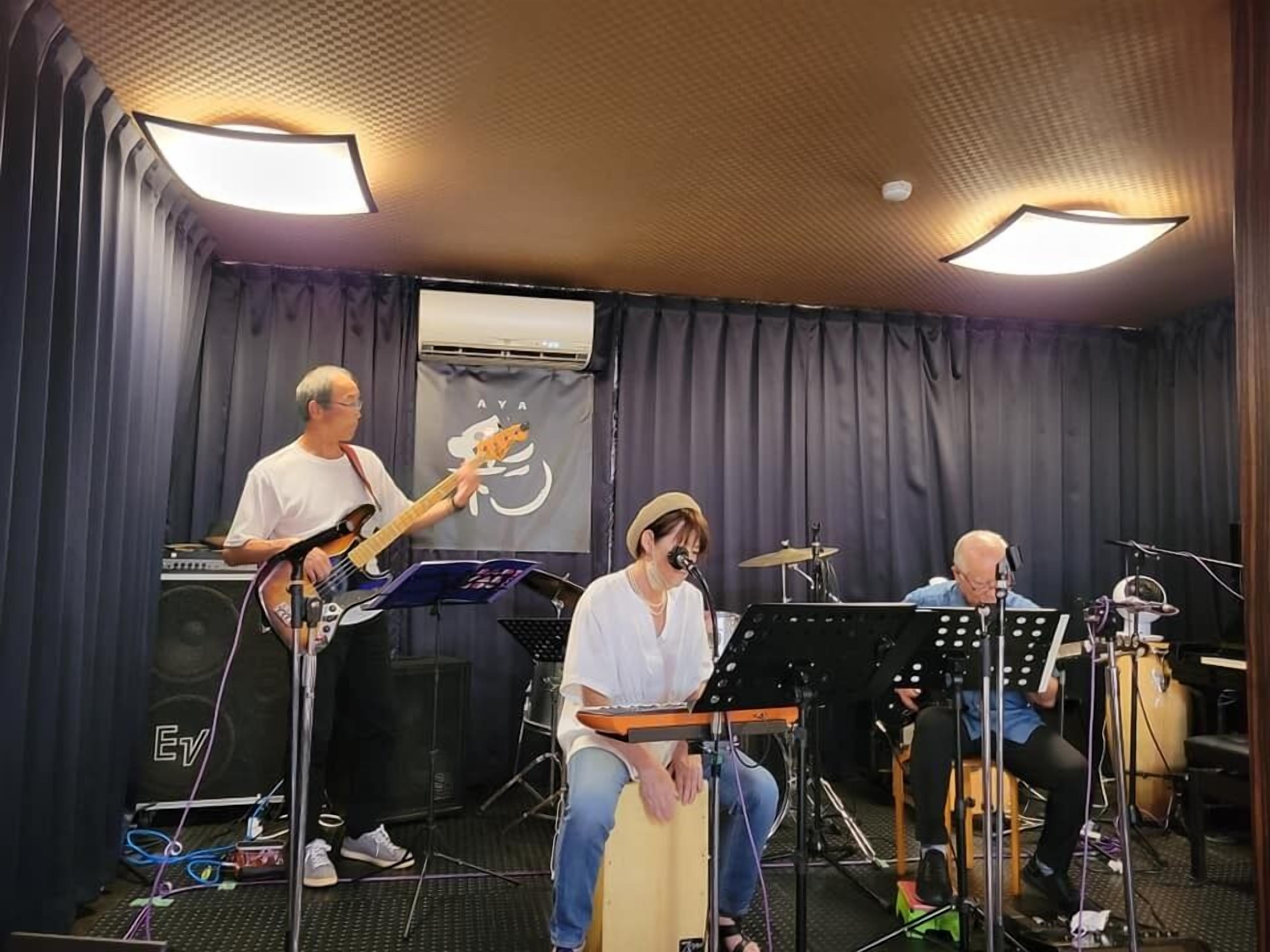 A band performing in a room with a stage, musical instruments, and a curtain backdrop.