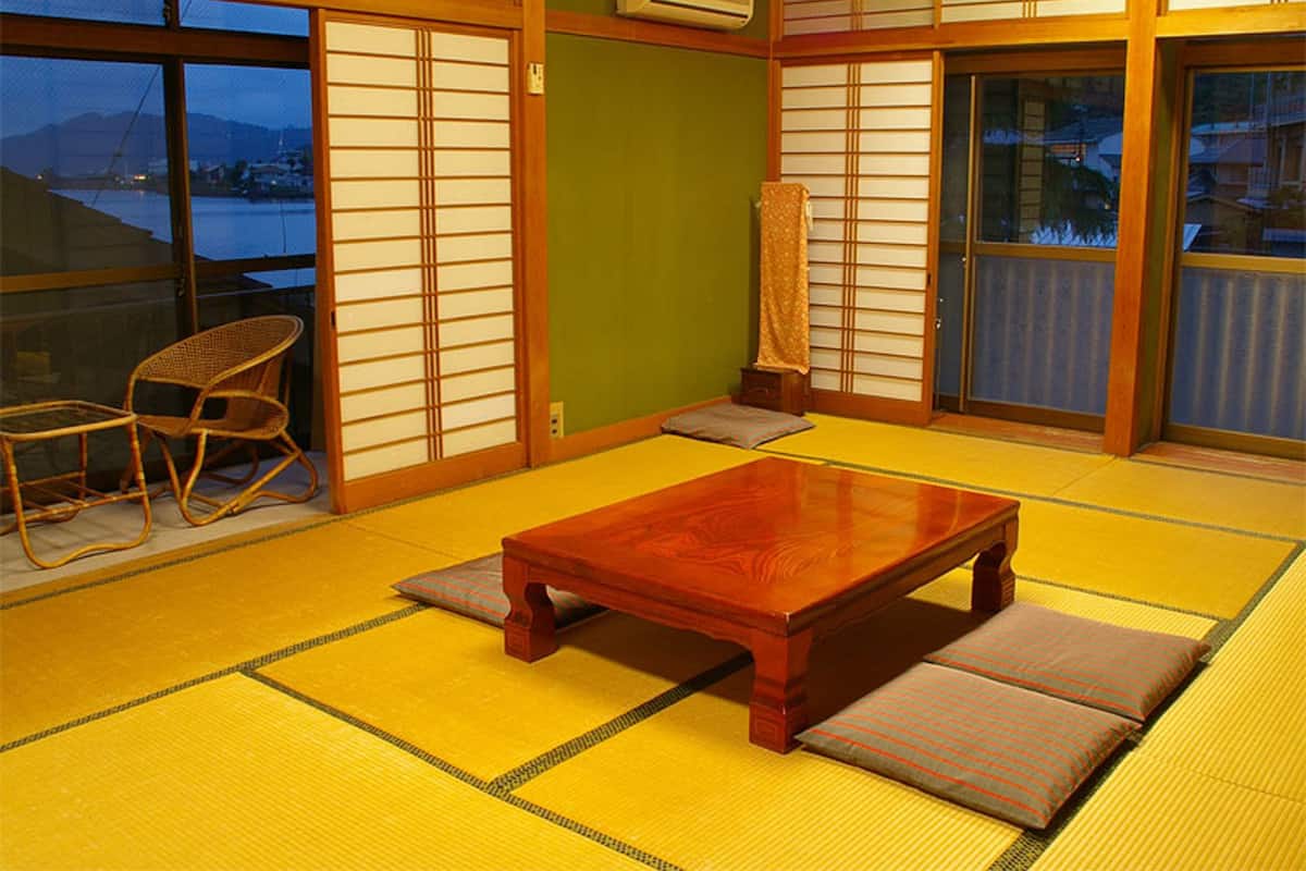 A traditional Japanese room with tatami flooring, a wooden table, a chair, sliding doors, and a view of a body of water.