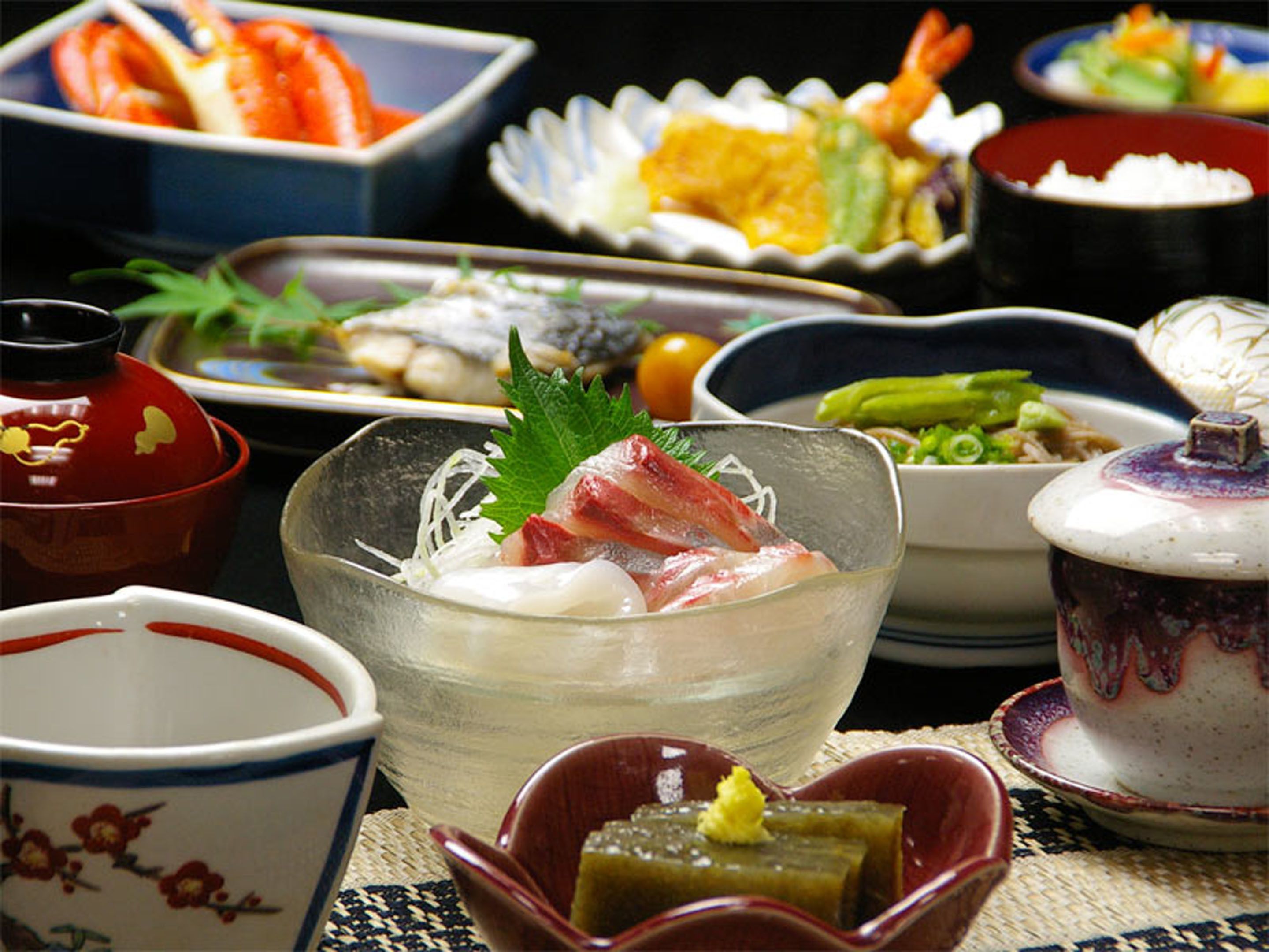 A variety of Japanese dishes, including sashimi and sushi, served on traditional ceramic dishes.