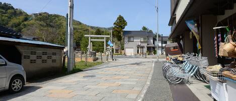 A street with a white car parked on the left, a row of bicycles on the right, and a building with a sign in the background.