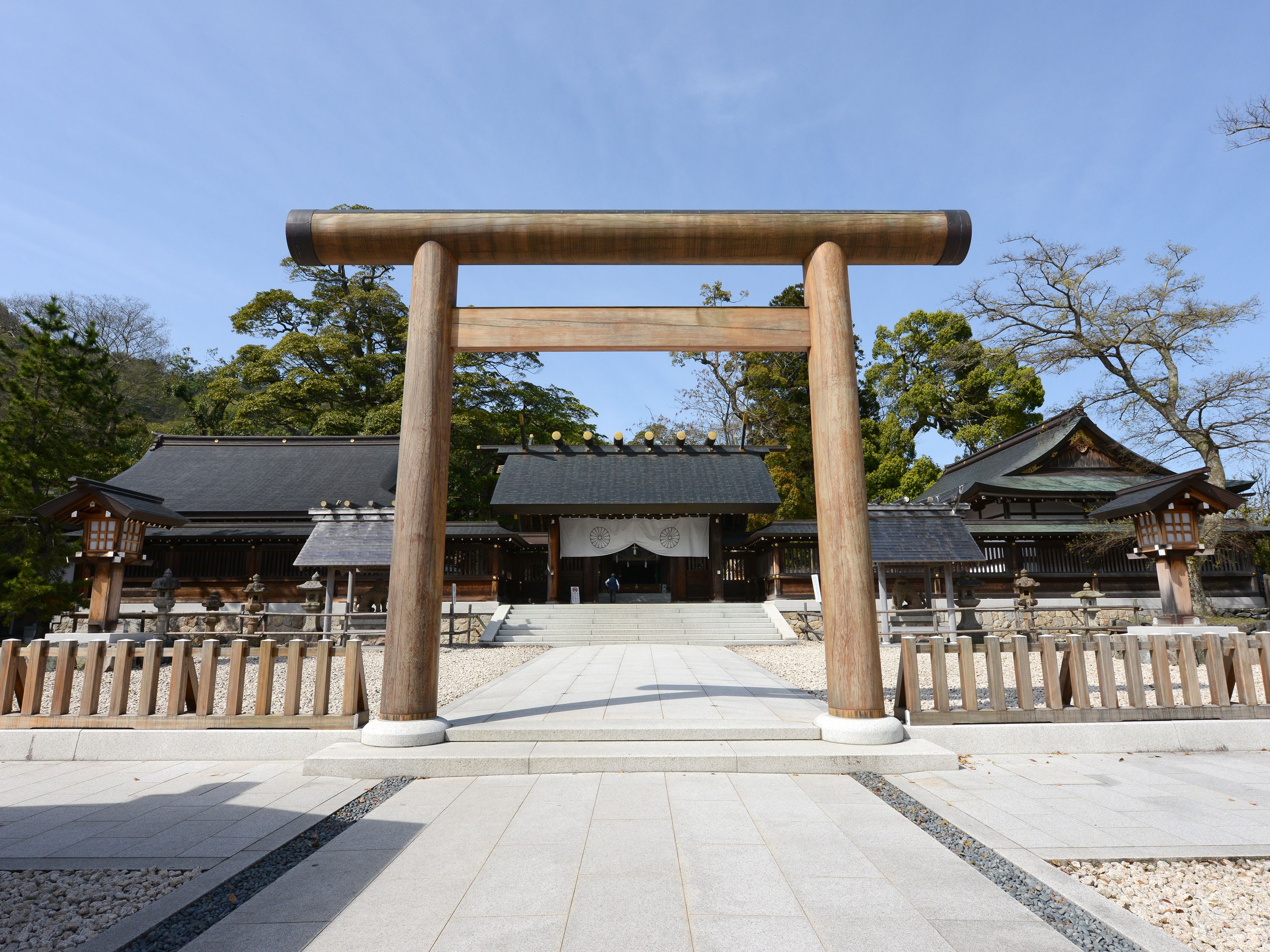 Ein traditionelles japanisches Torii-Tor, das zu einem Tempelkomplex mit Holzbauten und einem Steinweg führt.