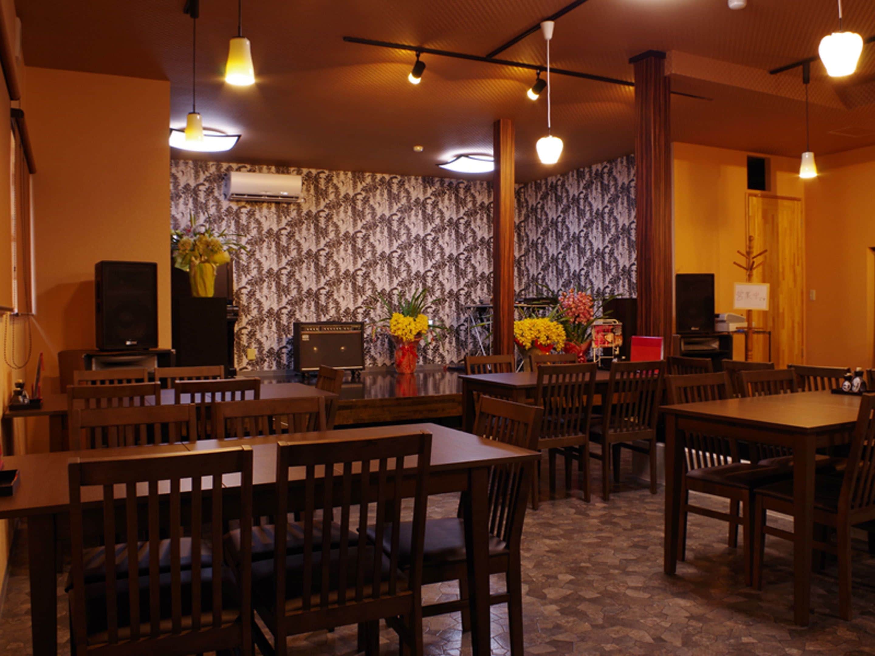 A restaurant with wooden tables and chairs, a patterned wallpaper wall, and hanging pendant lights.