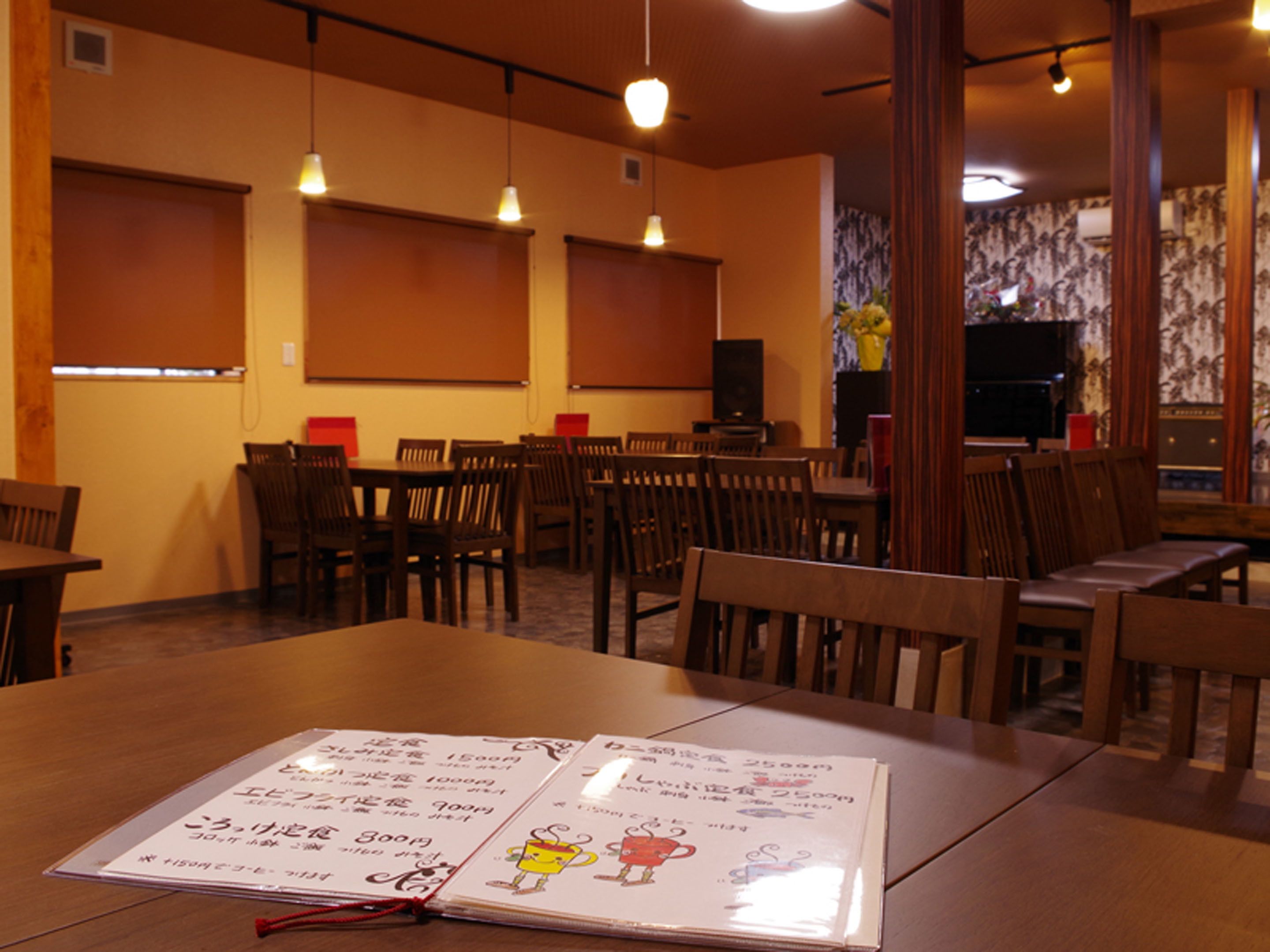 A restaurant interior with wooden tables and chairs, pendant lighting, and a menu on the table.