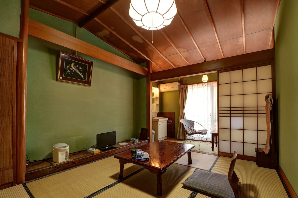 A traditional Japanese room with tatami flooring, a low wooden table, a television, and a futon bed.