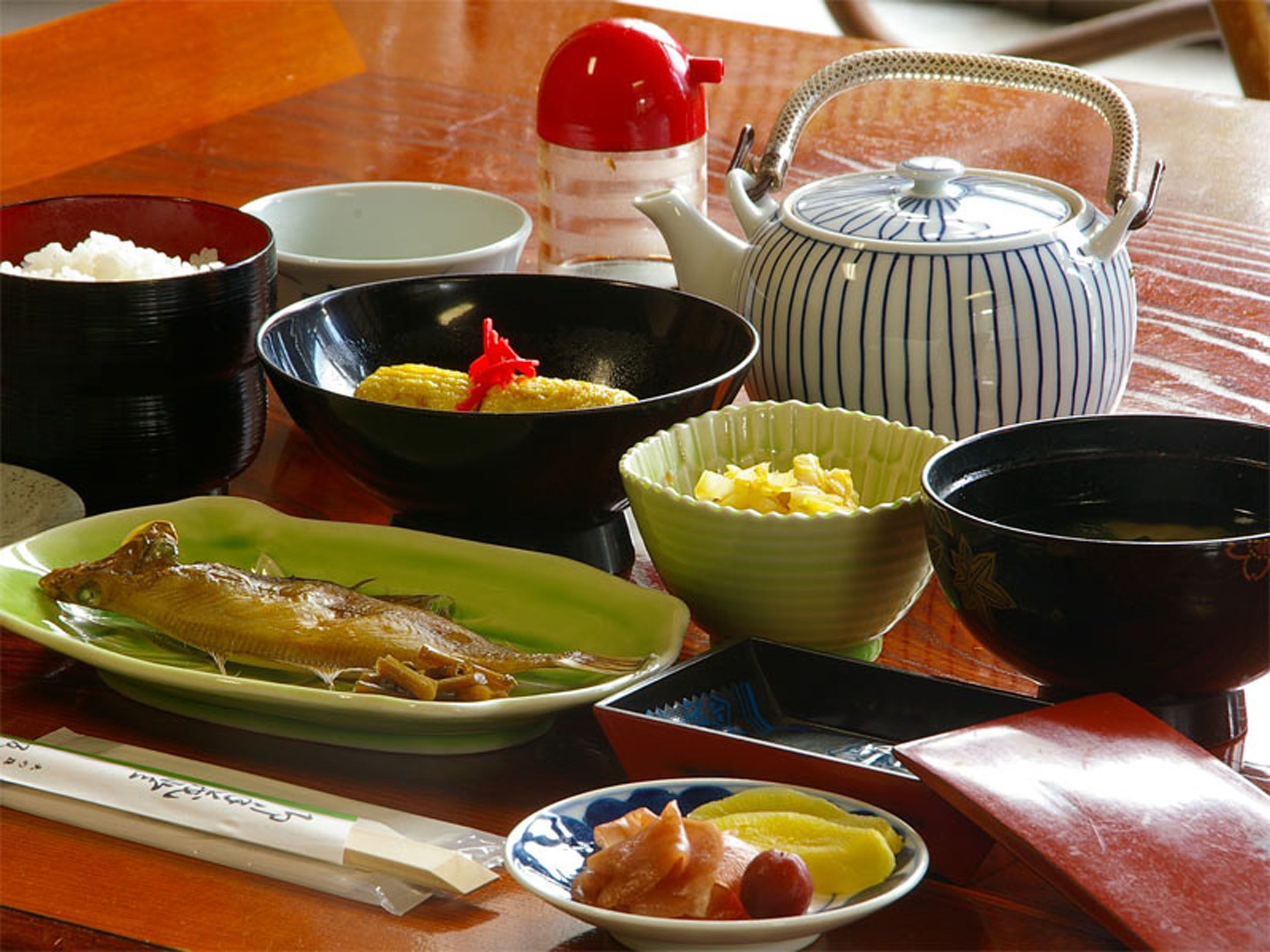 A table with various dishes, including fish, vegetables, and a teapot.