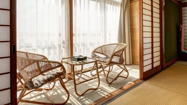 Une pièce de style japonais traditionnel, avec un sol recouvert de tatamis, une table basse, deux chaises en osier et des paravents en papier de riz (shoji).