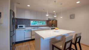 A modern kitchen with white cabinetry, a central island, and pendant lighting. - Holiday Niseko Shiki and Koyuki (Kutchan)