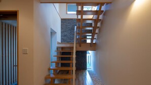 A modern interior with a wooden staircase, stone wall, and a view of the outdoors. - Holiday Niseko Shiki and Koyuki (Kutchan)