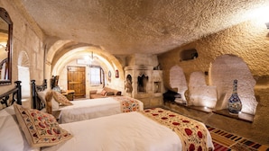 A room with two beds, a wooden bench, a stone fireplace, and a large vase on a shelf. - Tulip Cave Suites (Nevsehir)