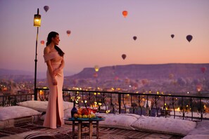 A balcony with a table set for two, overlooking a cityscape with hot air balloons. - Tulip Cave Suites (Nevsehir)