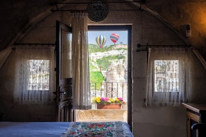 A room with a balcony, a bed, a window with curtains, and a view of hot air balloons. - Tulip Cave Suites (Nevsehir)