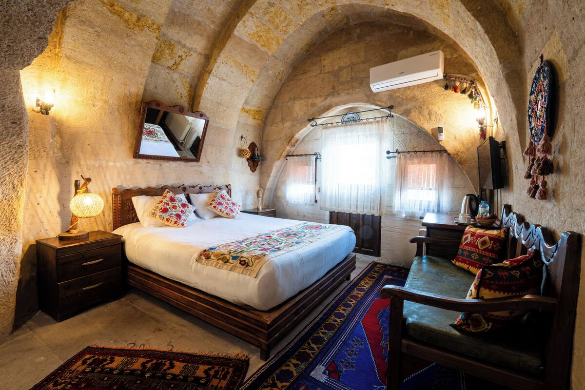 Un dormitorio con cama, mesitas de noche, escritorio, silla, espejo y ventana con cortinas.