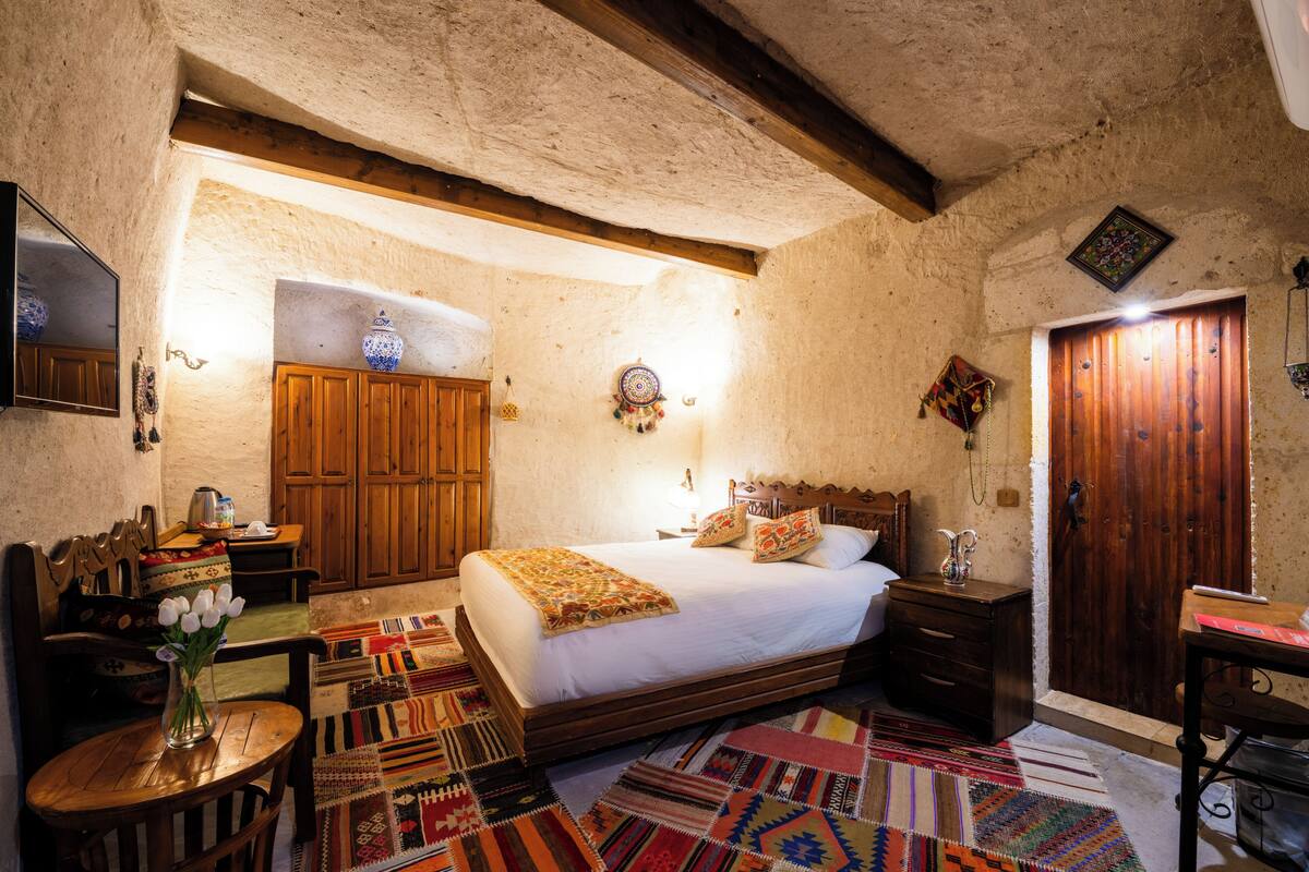 Un dormitorio con una cama de madera, una mesita con un florero y una alfombra estampada.