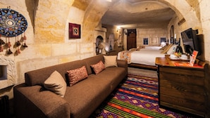 A room with a sofa, a bed, a wooden dresser, and a colorful carpet. - Tulip Cave Suites (Nevsehir)
