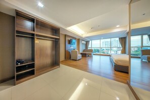 A hotel room with a large bed, a seating area, a wardrobe, and a view of the city. - Top View Hotel (Si Racha)