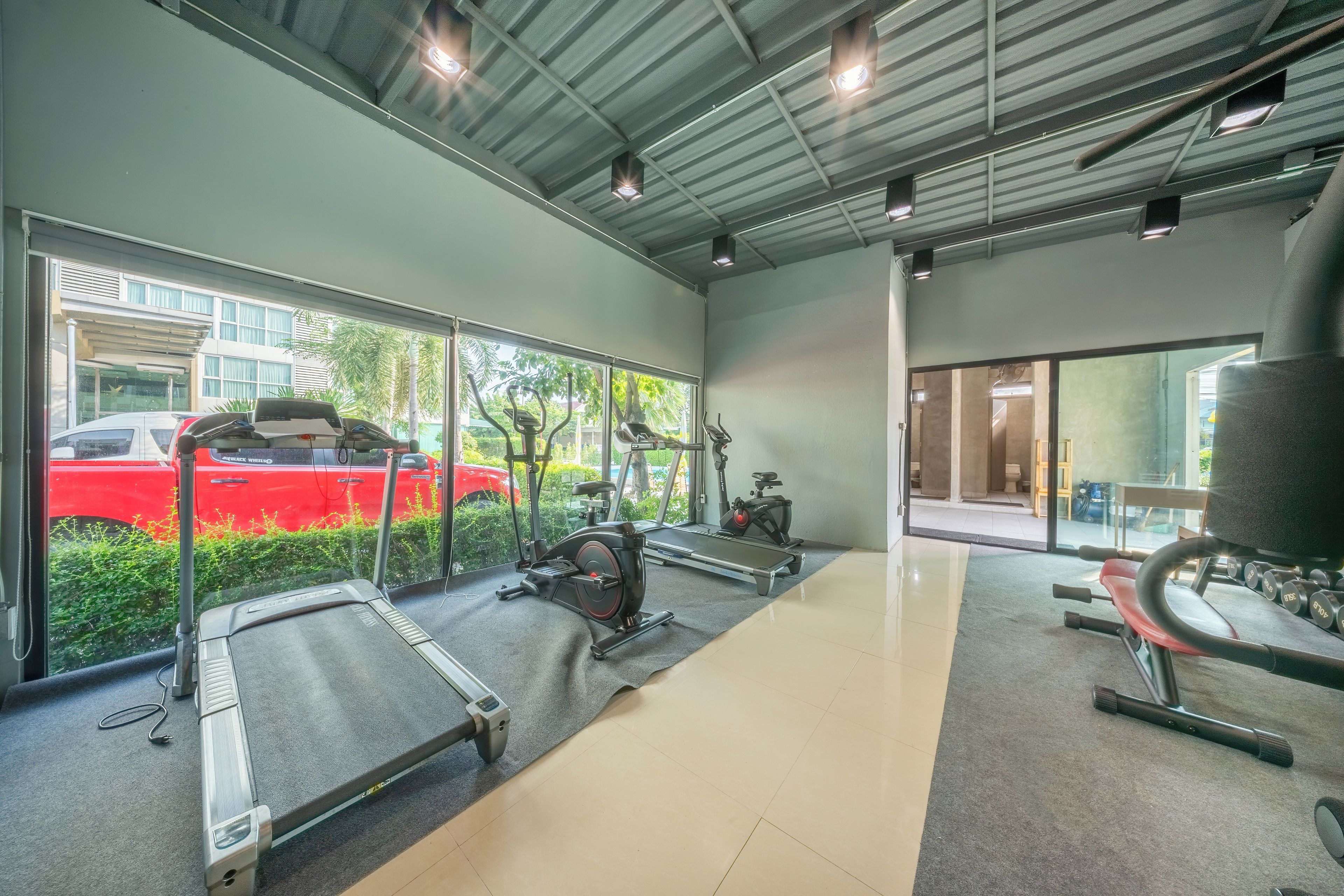 Ein Fitnessstudio mit Trainingsgeräten, einem Laufband und einem roten Auto davor.