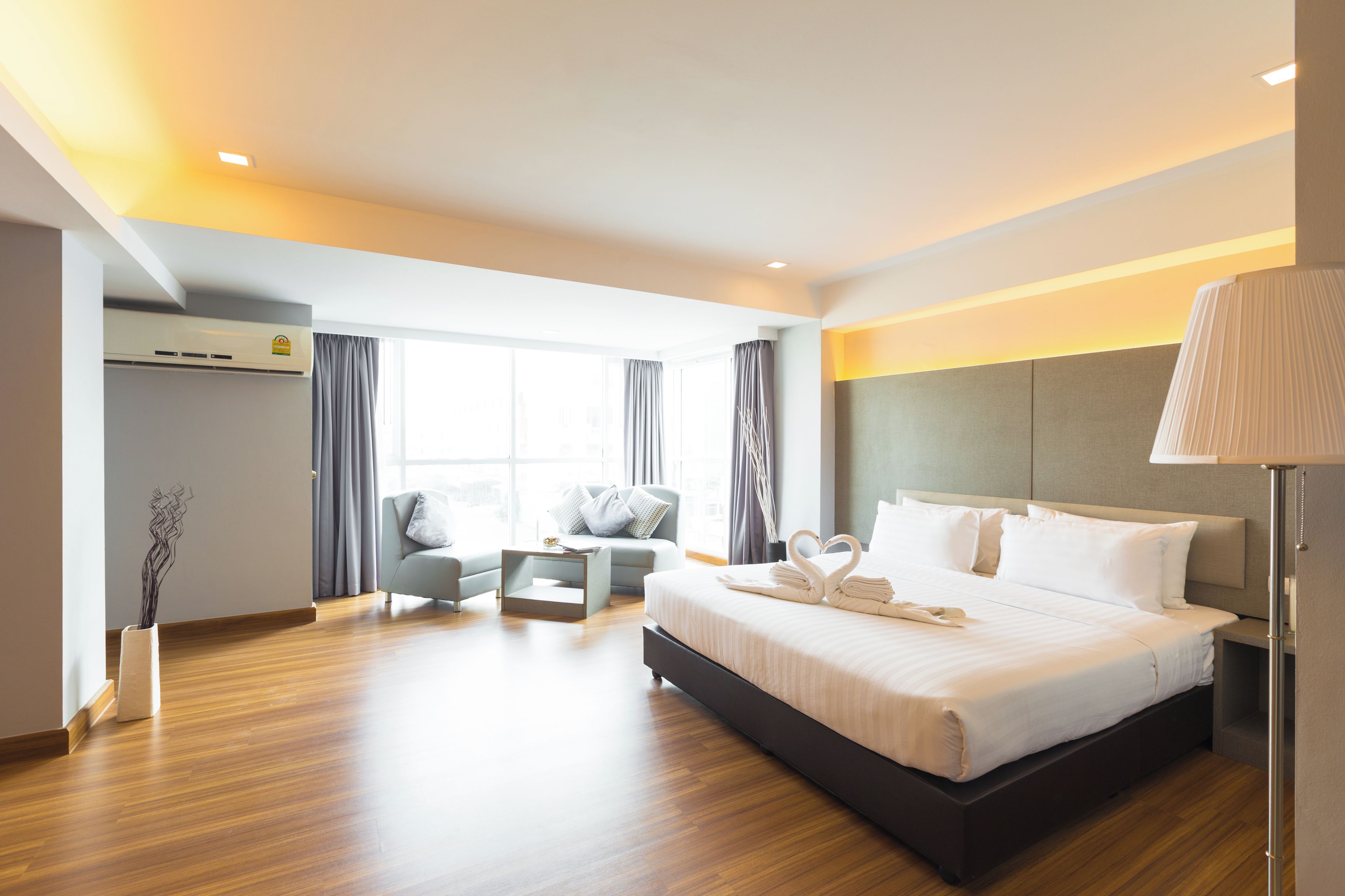 A modern hotel room with a large bed, a seating area with a sofa and armchairs, a flat-screen TV, and a large window.