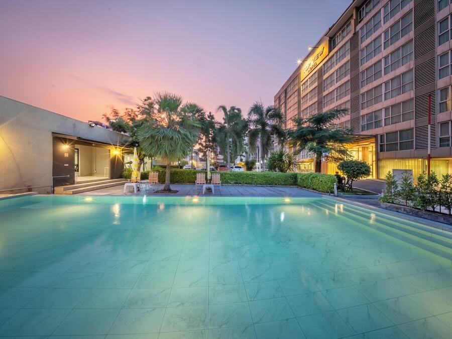 Zona de piscina de hotel con cielo despejado, palmeras y un edificio con un letrero.
