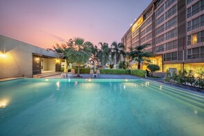 A hotel pool area with a clear sky, palm trees, and a building with a sign. - Top View Hotel (Si Racha)