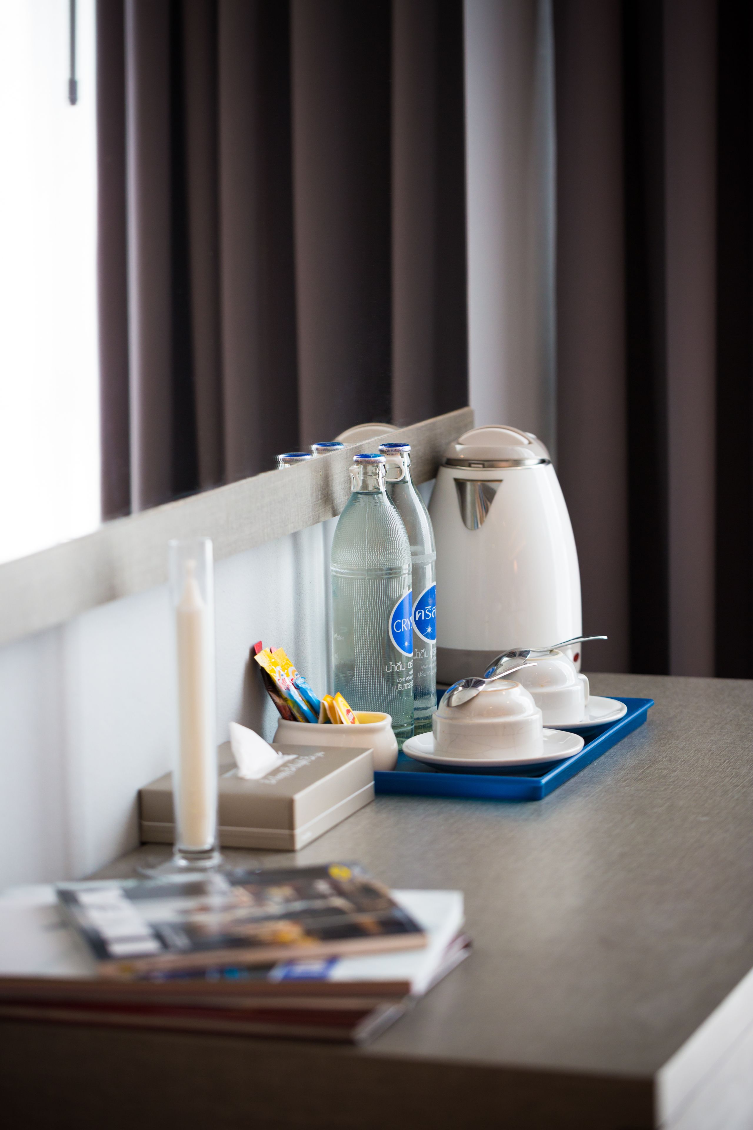 A neatly arranged hotel room with a breakfast tray, a bottle of water, a coffee maker, and a glass of milk on the table.