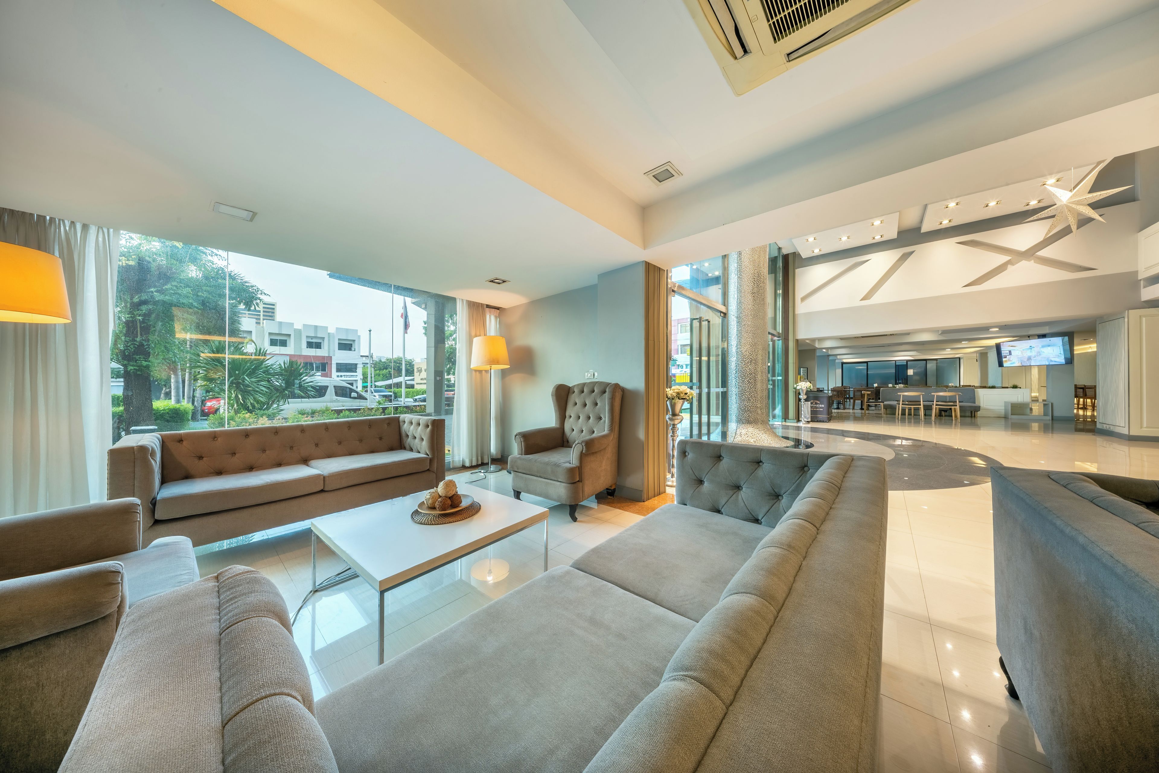 A modern hotel lobby with a sofa, armchairs, a coffee table, and a large window offering a view of the city.