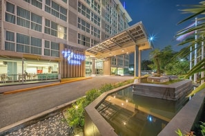 Entrada de hotel con diseño moderno, un paseo techado y un pequeño elemento acuático.
