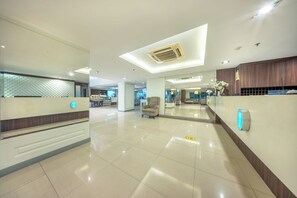 Un hall de hotel con una recepción, área de descanso y un diseño de techo moderno.