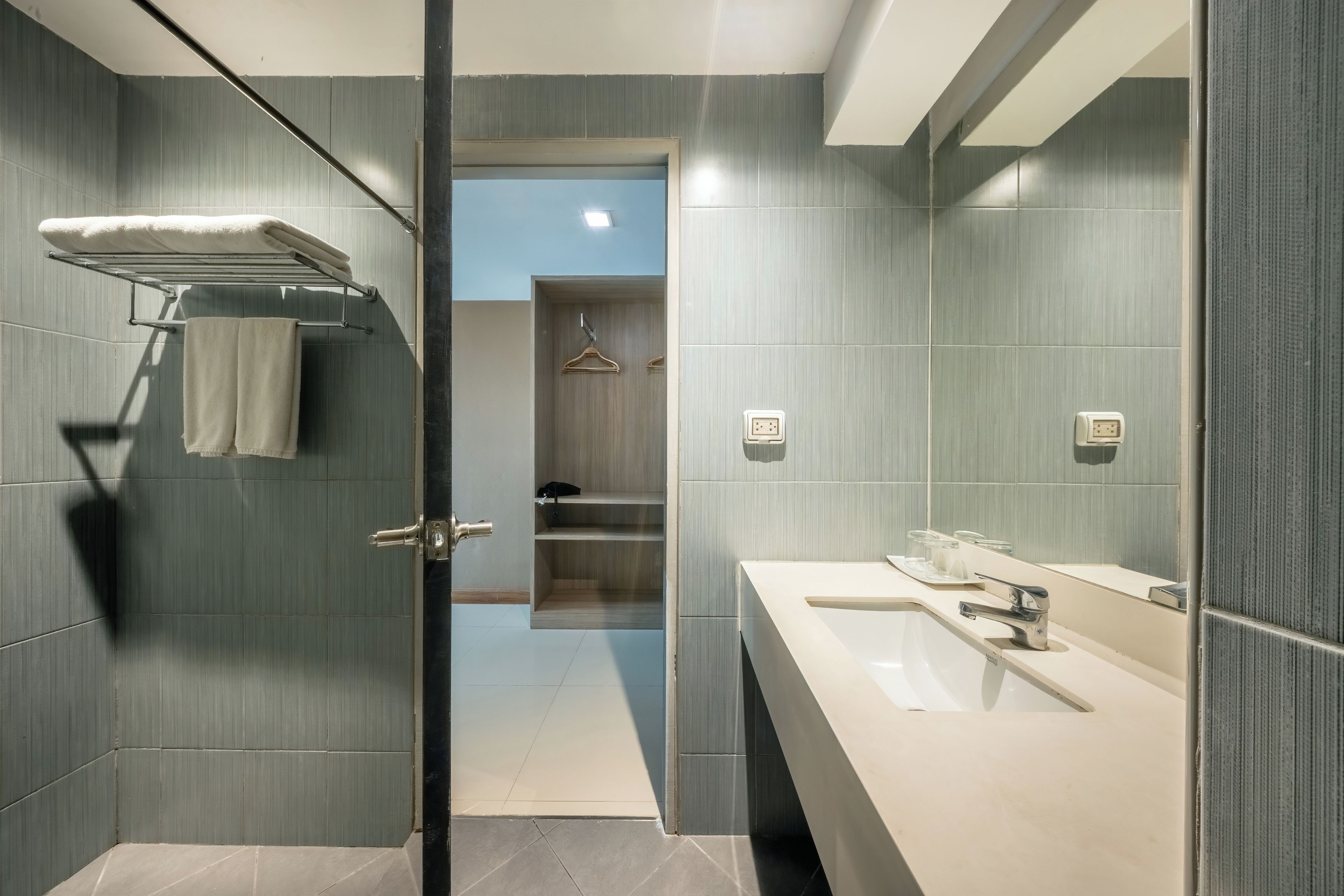 Un baño moderno con entrada de puerta de cristal, un perchero, un lavabo y un espejo.