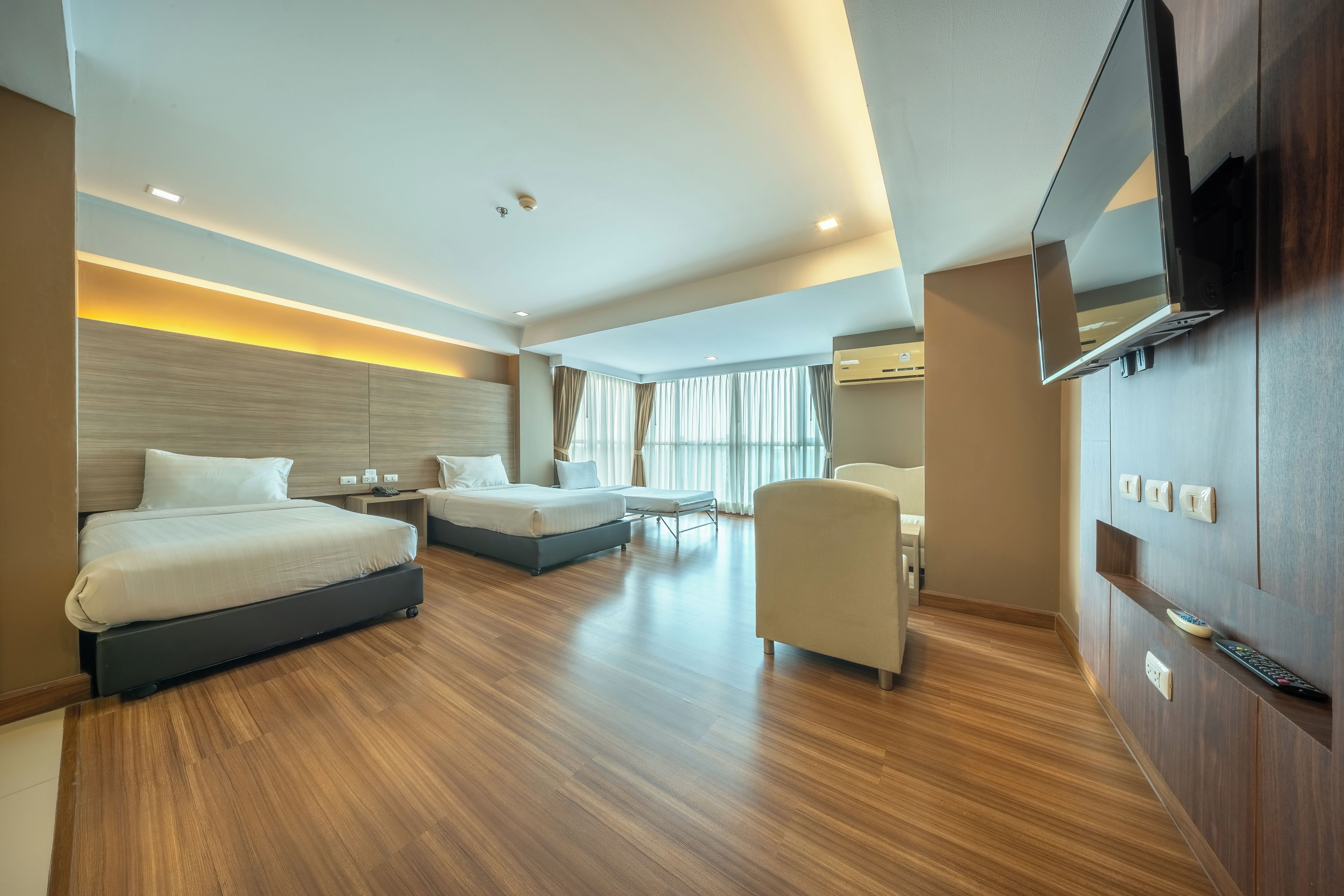 Ein modernes Hotelzimmer mit einem großen Bett, einem kleineren Bett, einem Sofa, einem Fernseher und einem Schreibtisch.