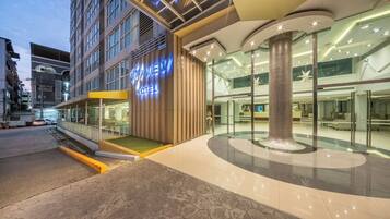 Fachada de hotel con diseño moderno, que presenta vidrio, una columna central y un interior bien iluminado.