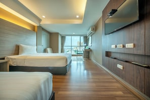 A hotel room with two beds, a desk, a chair, a TV, and a view of the city. - Top View Hotel (Si Racha)