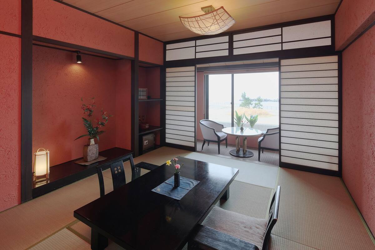 A traditional Japanese room with tatami flooring, a dark wooden table, and a sliding door leading to a balcony with a view.