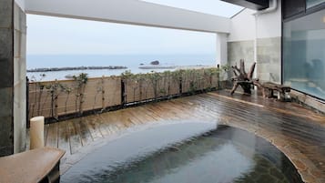 A wooden deck with a stone pool, overlooking a calm sea with rocky outcrops.