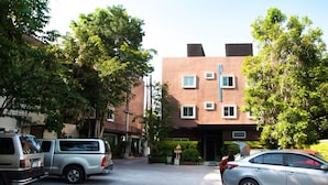 A parking area with a silver car and a silver pickup truck. There is a building with multiple windows and a brown facade. - Pova Residence and Boutiques Resort (Chonburi)