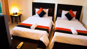 A hotel room with two beds, each with white bedding and red and black accents. There is a nightstand with a lamp and a remote control on the floor.
