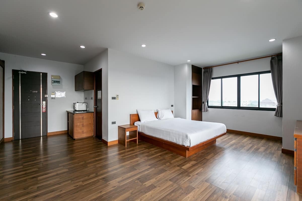 A modern hotel room with a wooden floor, a large bed, a desk, and a window with curtains.