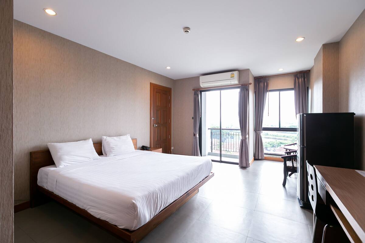 A hotel room with a large bed, a desk, a television, and a balcony with a view.