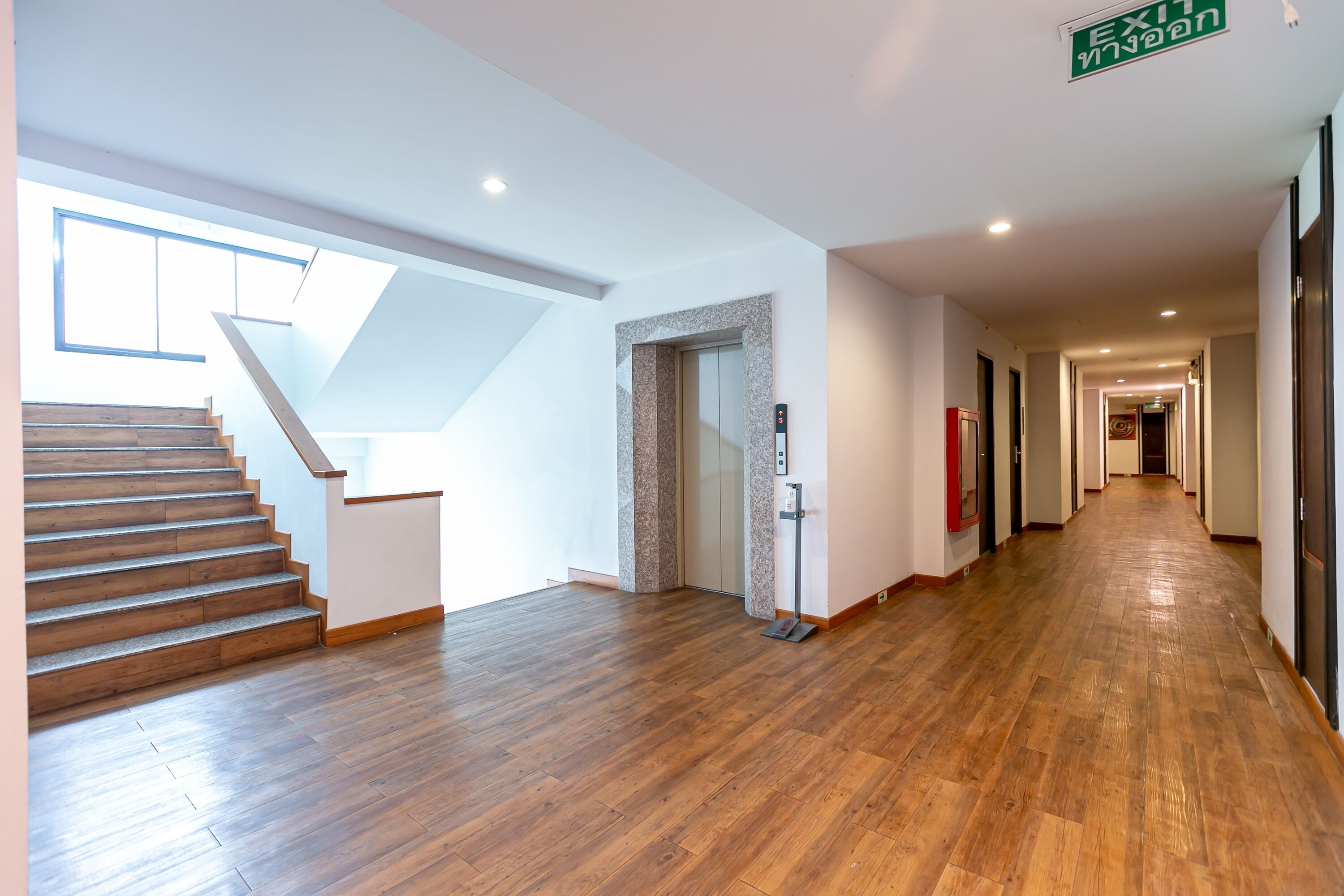 A hotel hallway with wooden flooring, a staircase, and an elevator.