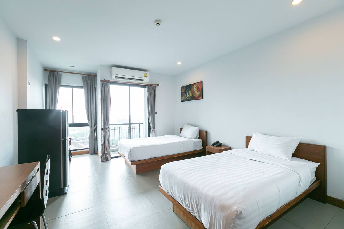 A hotel room with two beds, a desk, a wardrobe, and a balcony with curtains.