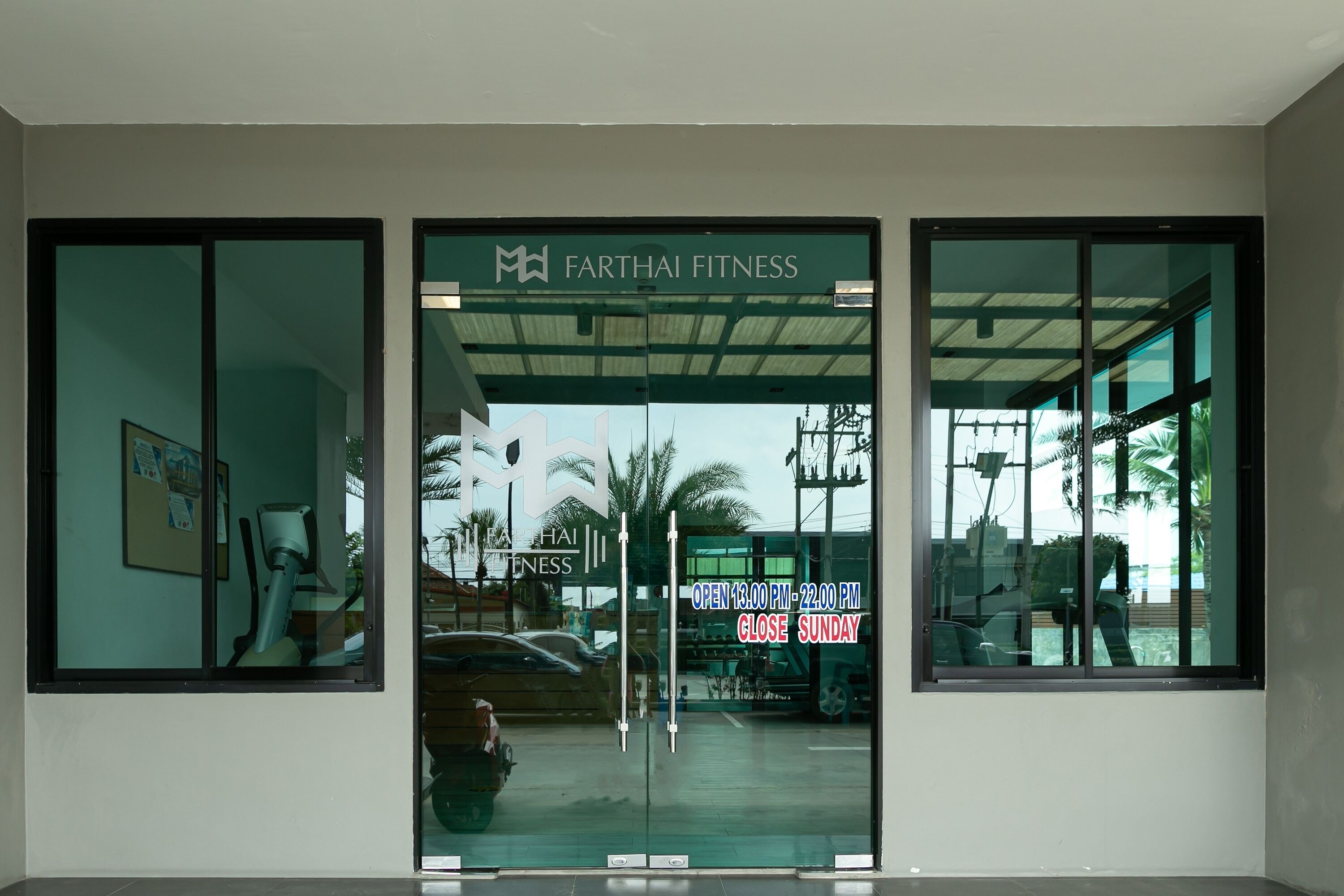 Entrada de un gimnasio con un cartel que dice 'Farthai Fitness' y el horario de atención.