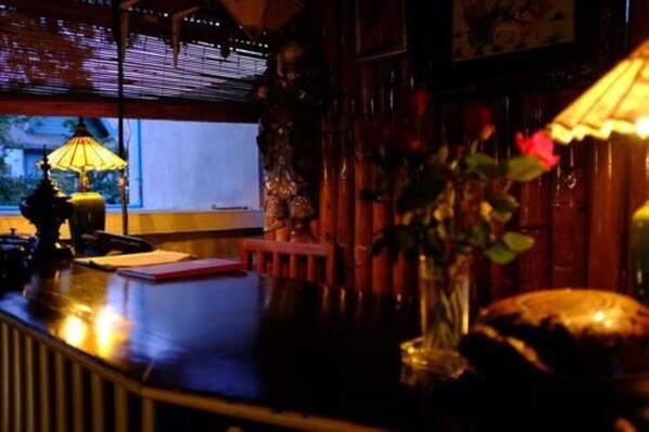 A dimly lit room with a wooden desk, a lamp, and a vase with flowers. - Palace Nyaung Shwe Guest House (Nyaungshwe)
