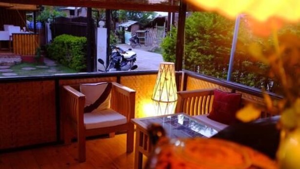 A room with a wooden floor, a table with a glass top, a chair with a cushion, and a lamp.