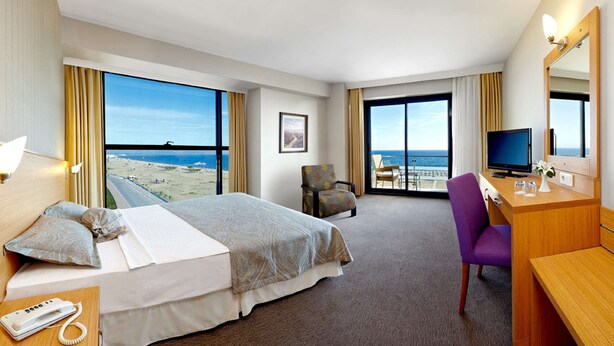 A hotel room with a bed, a desk, a chair, a TV, and a view of the ocean. - Ayvalik Cinar Hotel (Ayvalik)
